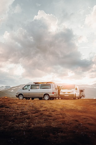A panoramic shot of a fleet of polished caravans parked against a backdrop of rolling hills at sunset.
