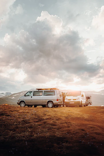 A couple standing beside their camper van overlooking a lush green valley at sunset.