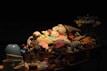 A collection of hand-knitted stuffed animals is arranged in wicker baskets, brightly colored and illuminated against a dark background. The toys include various animals wearing cute outfits, giving a cozy and inviting feel. Nearby, there are other plush toys on a display stand, as well as some ceramic bowls in the foreground.