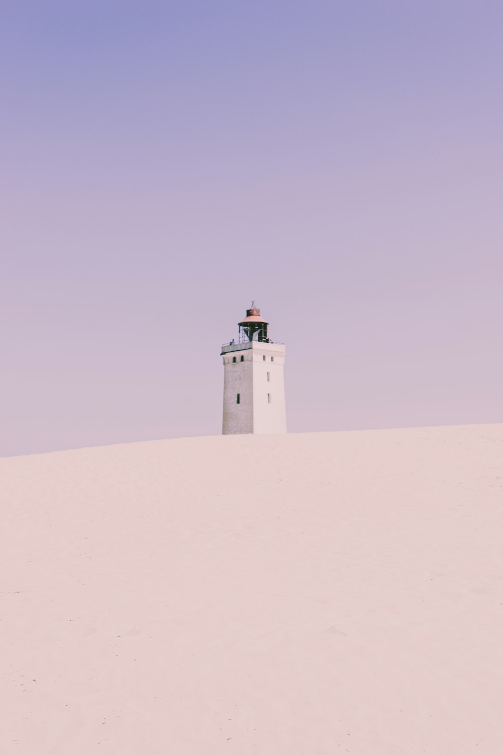 昼間の白い砂浜に白いコンクリートの灯台