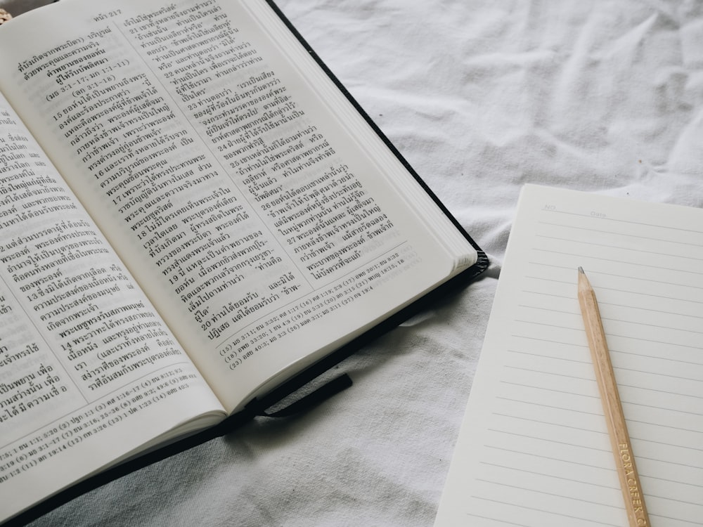 an open book and a pencil on a bed