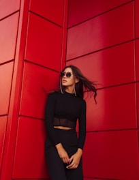 woman in black long sleeve shirt and black pants standing beside red wall