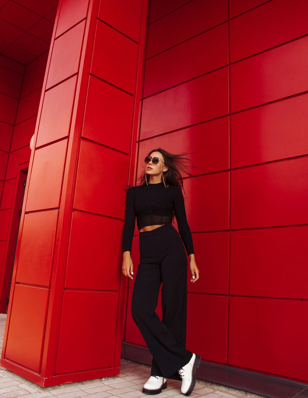 woman in black long sleeve shirt and black pants standing beside red wall