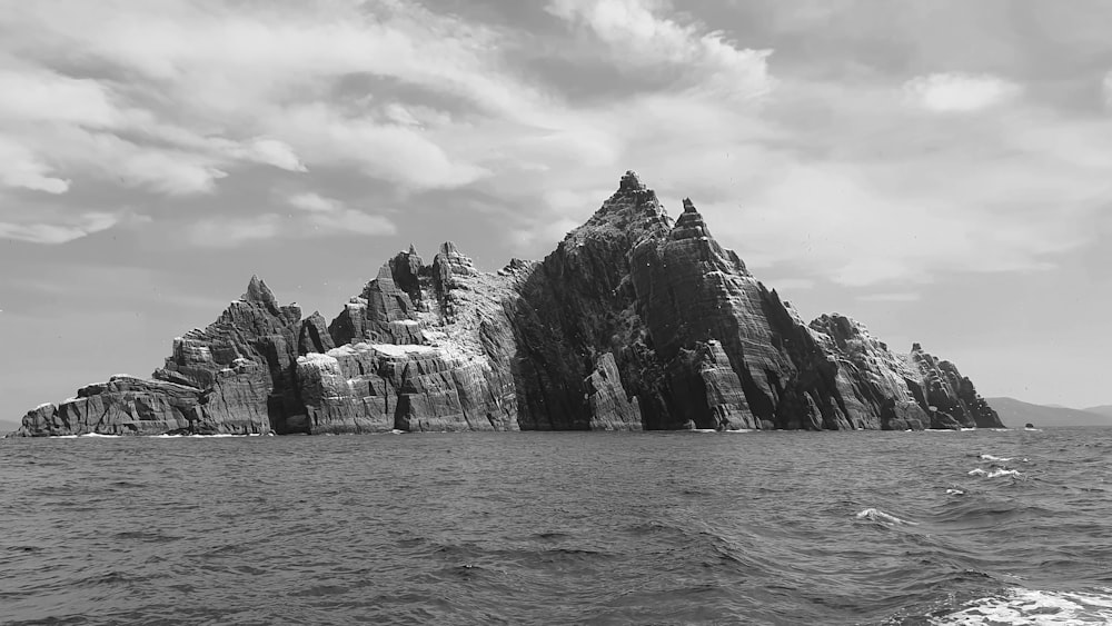 grayscale photo of rocky mountain near body of water