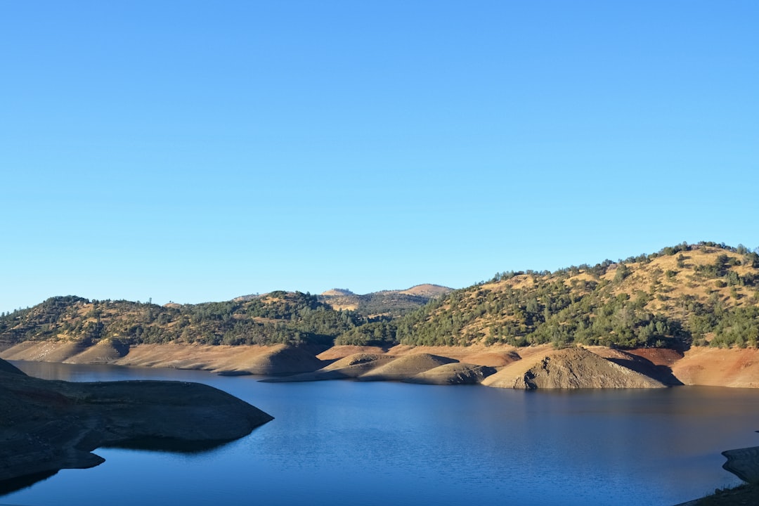 brown and green mountains beside blue lake under blue sky during daytime