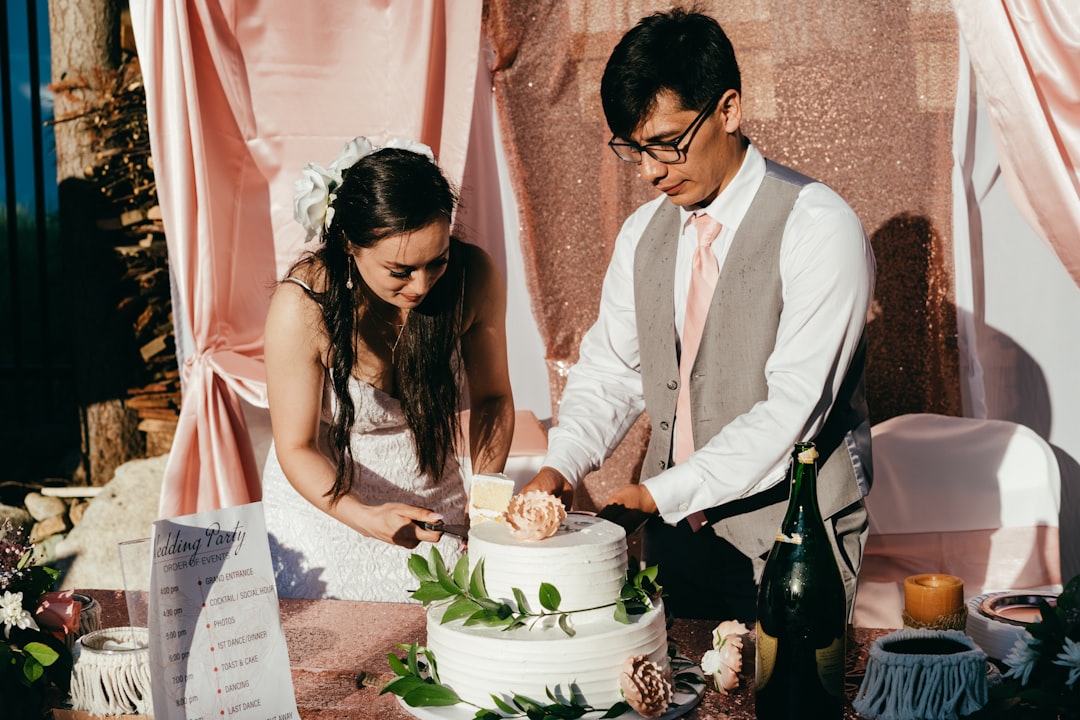 man in white dress shirt and woman in white sleeveless dress holding white and pink cake