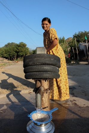 A smiling woman standing beside a newly installed water pump in a rural area.