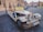 A vintage-style convertible car is parked on a cobblestone street in a historical area. The car is decorated with a sign offering sightseeing tours for 50 euros or 1200 CZK. There are buildings with classic architecture in the background along with a few pedestrians and parked cars.