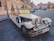 A vintage-style convertible car is parked on a cobblestone street in a historical area. The car is decorated with a sign offering sightseeing tours for 50 euros or 1200 CZK. There are buildings with classic architecture in the background along with a few pedestrians and parked cars.
