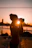 A candid photo of a smiling traveler holding a camera against a backdrop of a vibrant sunset beach.