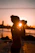 A candid photo of a smiling traveler holding a camera against a backdrop of a vibrant sunset beach.
