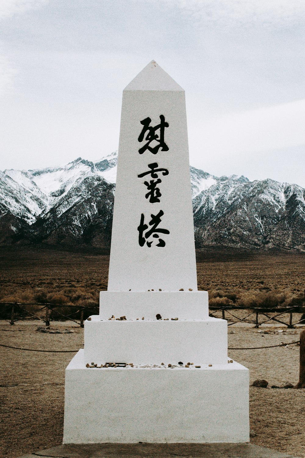 white concrete cross on brown field near snow covered mountain during daytime