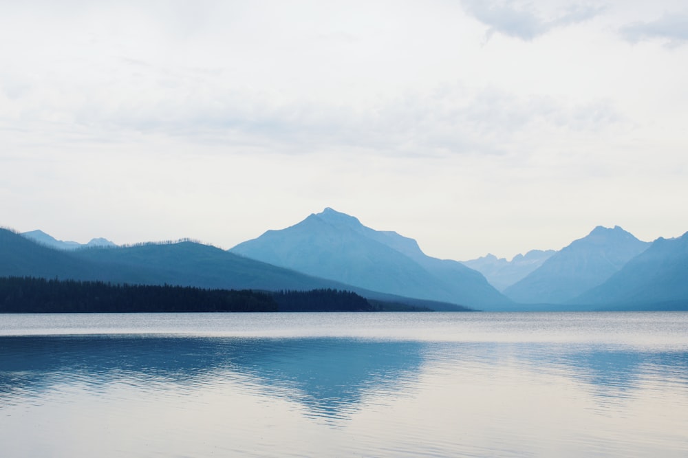 body of water near mountain under white sky during daytime