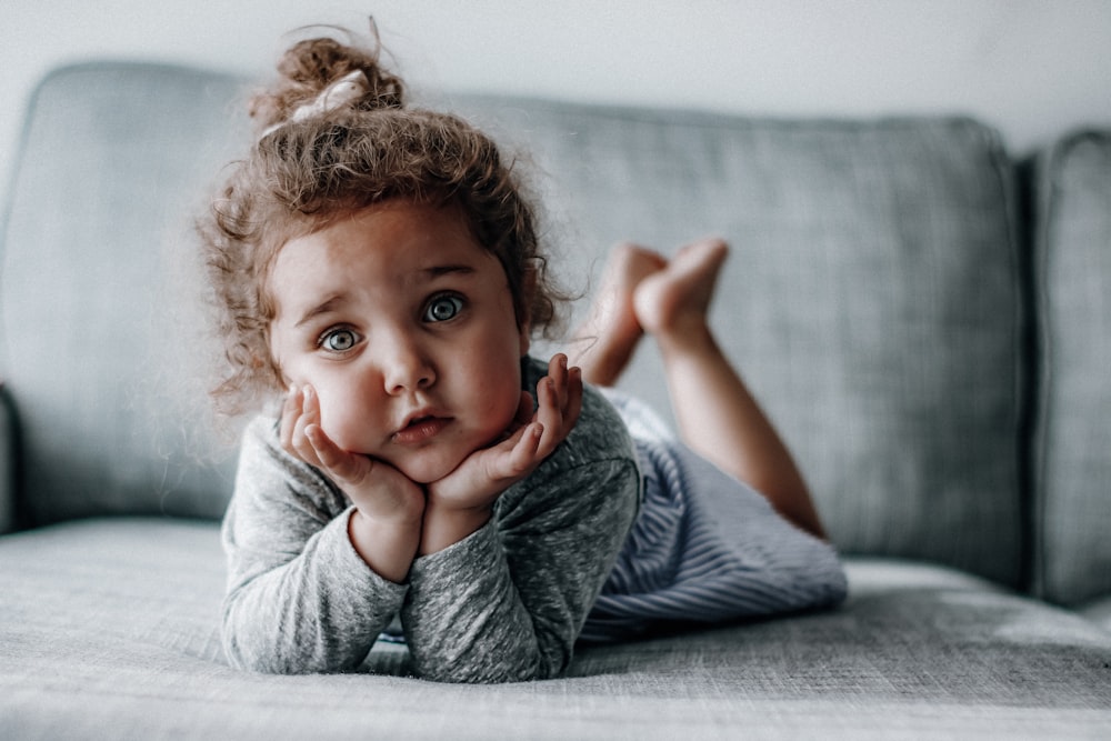 girl in gray long sleeve shirt lying on gray textile