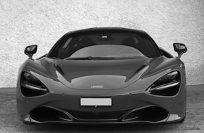 A sleek, high-performance sports car with an aerodynamic design and prominent features such as large headlights and a low profile. The car is parked on a brick surface with a textured wall in the background.