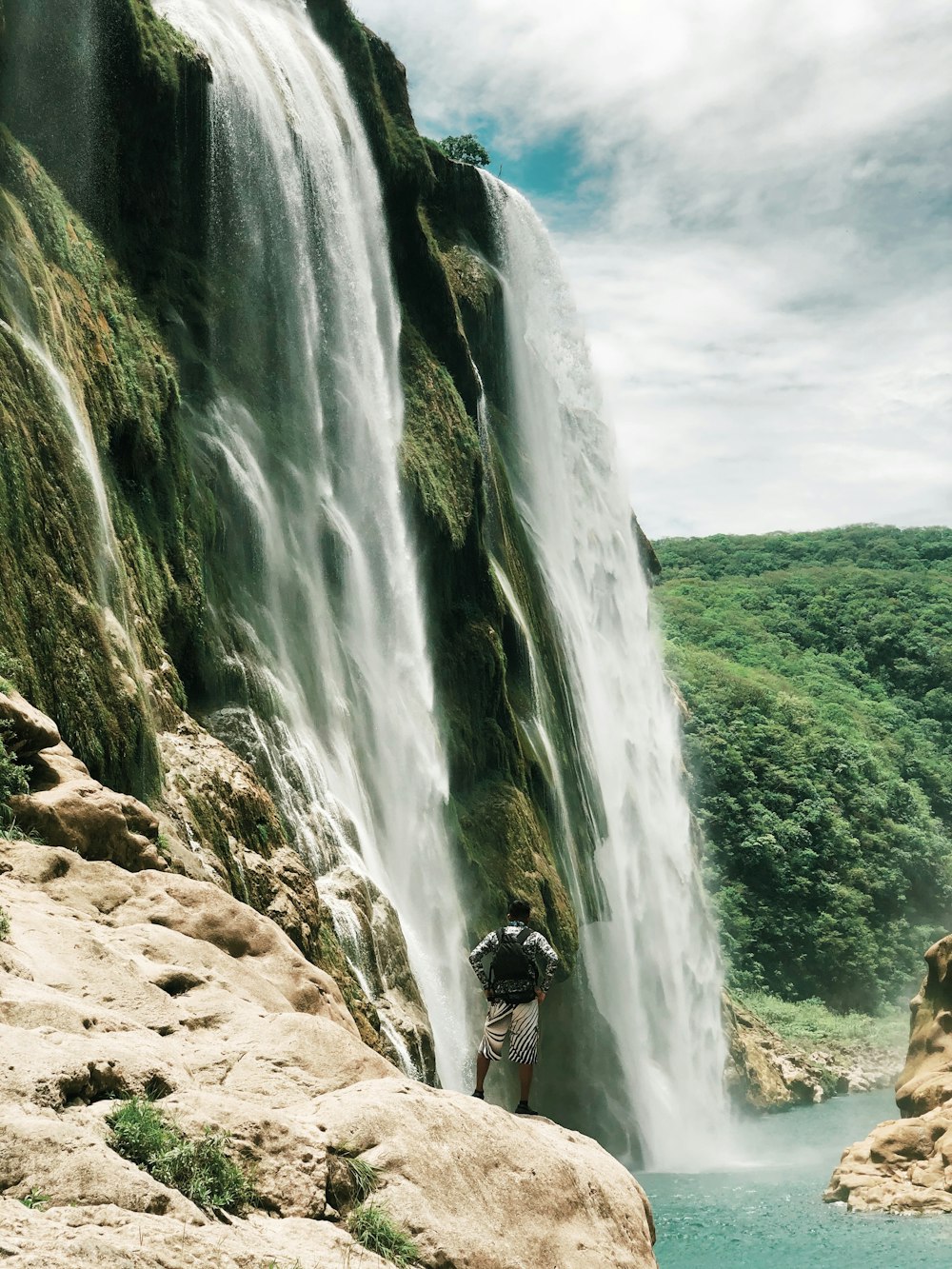 man in black jacket standing on brown rock near waterfalls during daytime