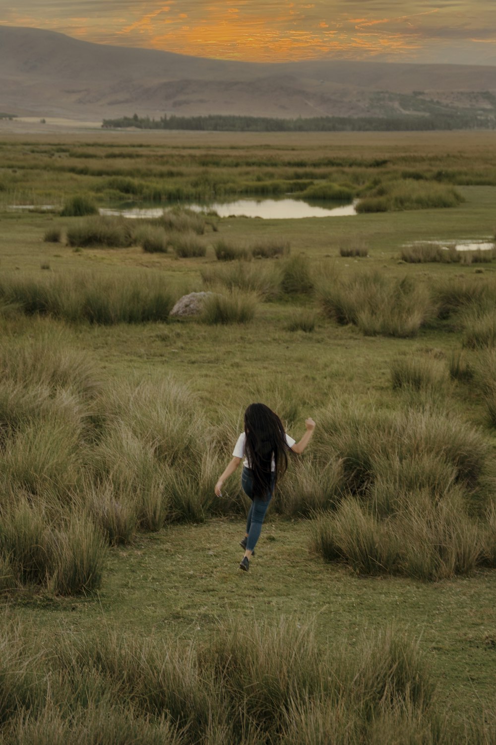 woman in black shirt and blue denim jeans walking on green grass field during daytime