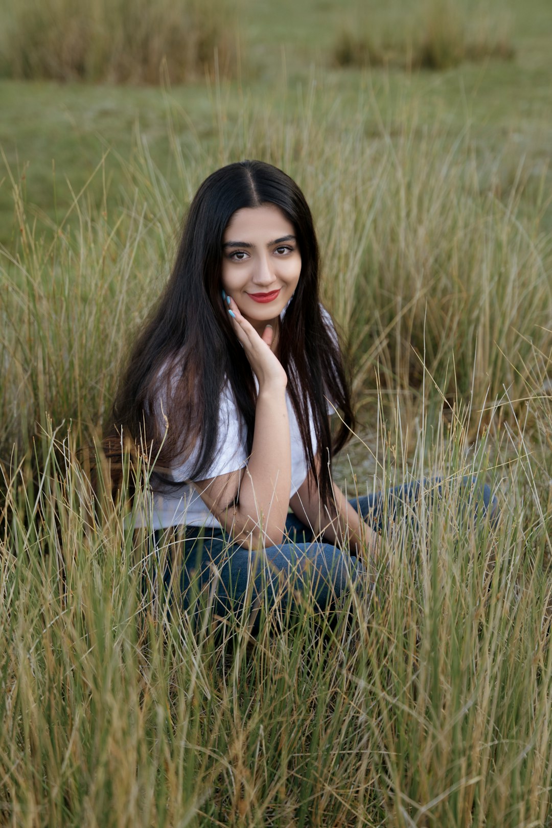 woman in white shirt and blue denim jeans sitting on green grass field during daytime