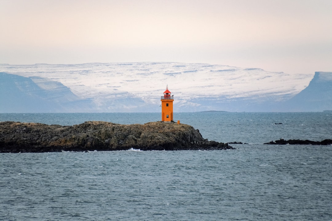 white and red lighthouse on brown rock formation near body of water during daytime