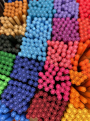 A close-up of colorful pens neatly arranged on a wooden desk.