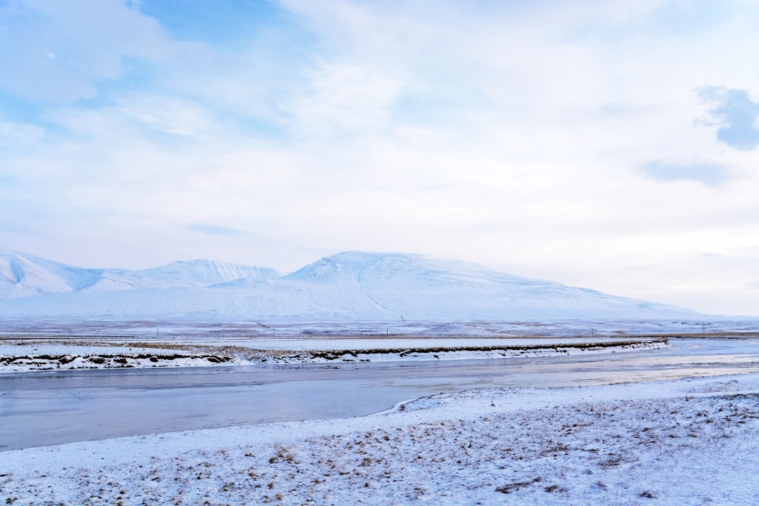 snow covered field near mountains under white clouds and blue sky during daytime