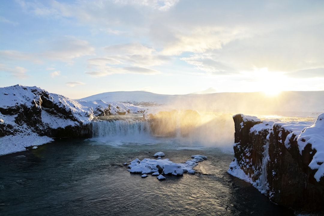 snow covered rocks on river under white clouds during daytime