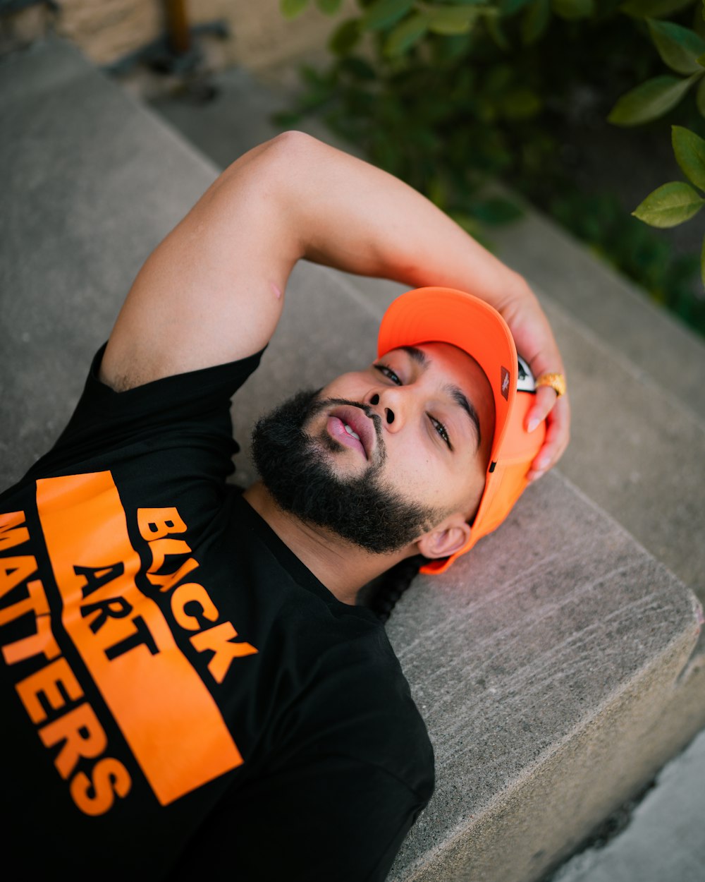 man in black and orange tank top lying on gray concrete floor