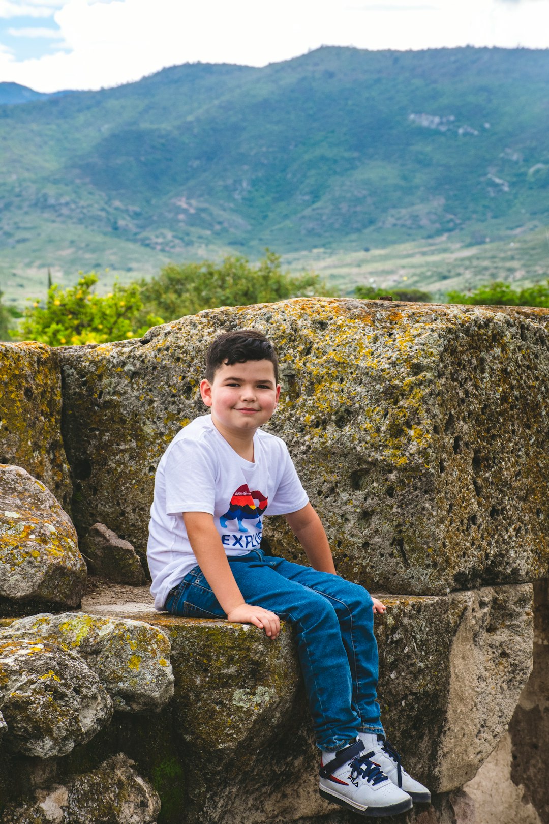 boy in white crew neck t-shirt and blue pants sitting on rock