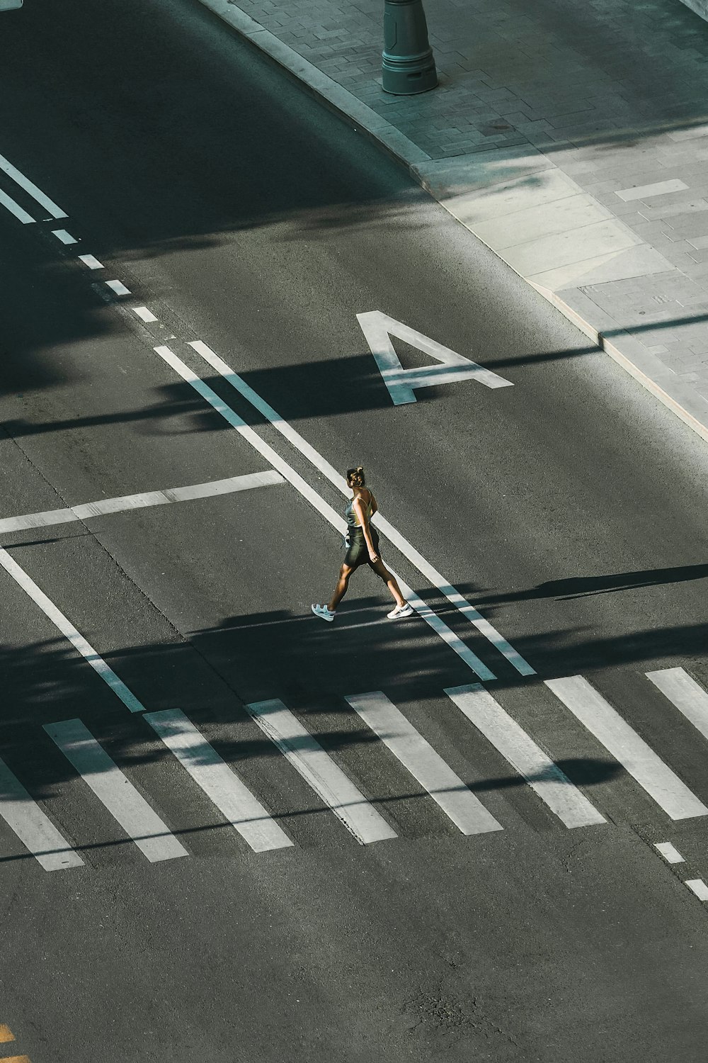 woman in white tank top and blue denim shorts walking on pedestrian lane during daytime