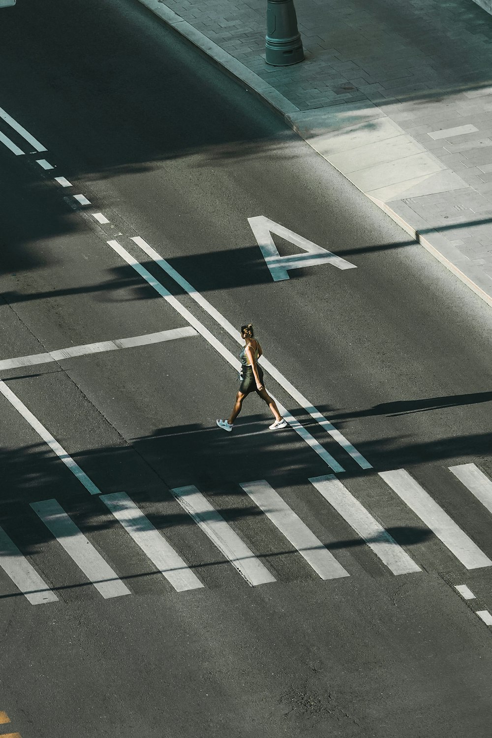 Mujer con camiseta blanca sin mangas y pantalones cortos de mezclilla azul caminando en el carril peatonal durante el día