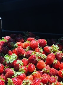 A collection of fresh, ripe strawberries with vibrant red hues and green stems, bathed in natural sunlight, creating a visually appealing array against a dark background.