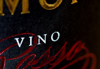Close-up of a wine label with prominently printed 'VINO' in white text. Surrounding it are larger golden letters partially visible and elegant red script text.