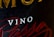Close-up of a wine label with prominently printed 'VINO' in white text. Surrounding it are larger golden letters partially visible and elegant red script text.