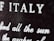 Close-up view of a textured surface with white text partially blurred. The letters are prominently visible, with 'ITALY' clearly noticeable.