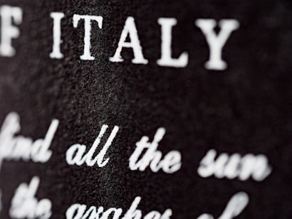 Close-up view of a textured surface with white text partially blurred. The letters are prominently visible, with 'ITALY' clearly noticeable.