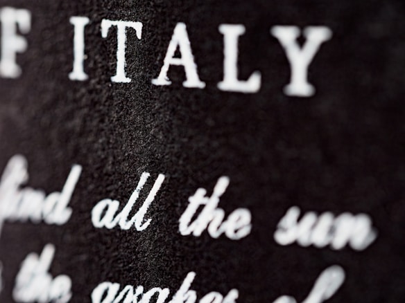 Close-up view of a textured surface with white text partially blurred. The letters are prominently visible, with 'ITALY' clearly noticeable.