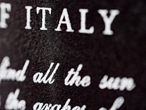 Close-up view of a textured surface with white text partially blurred. The letters are prominently visible, with 'ITALY' clearly noticeable.