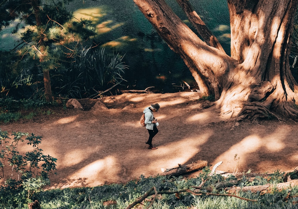 boy in white shirt and black pants walking on brown dirt road near green trees during