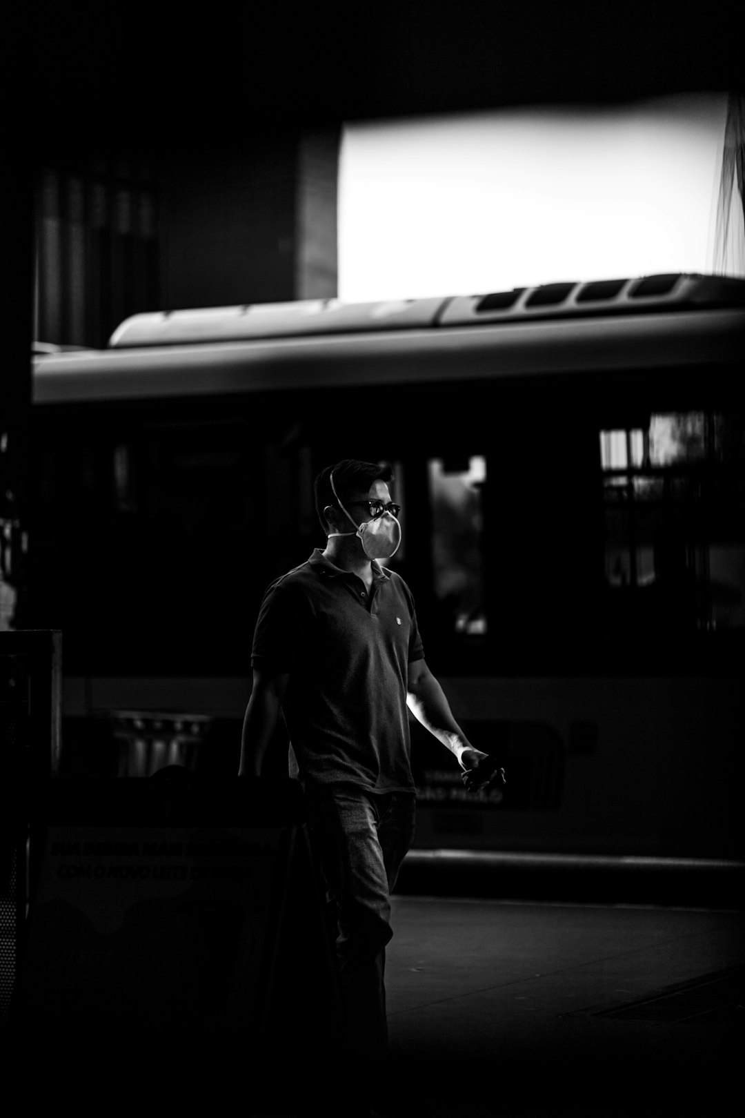 grayscale photo of man in black coat standing near train