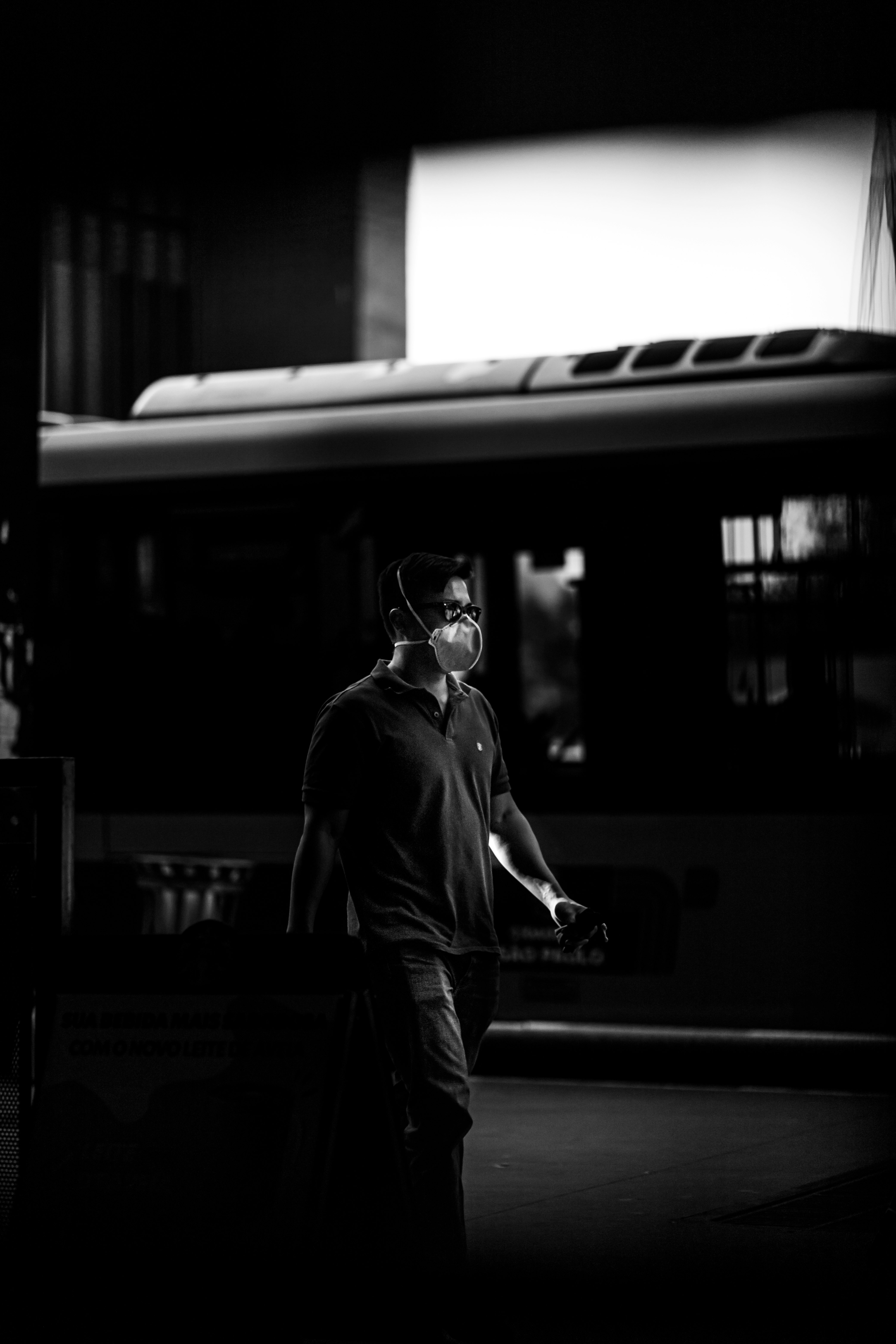 grayscale photo of man in black coat standing near train