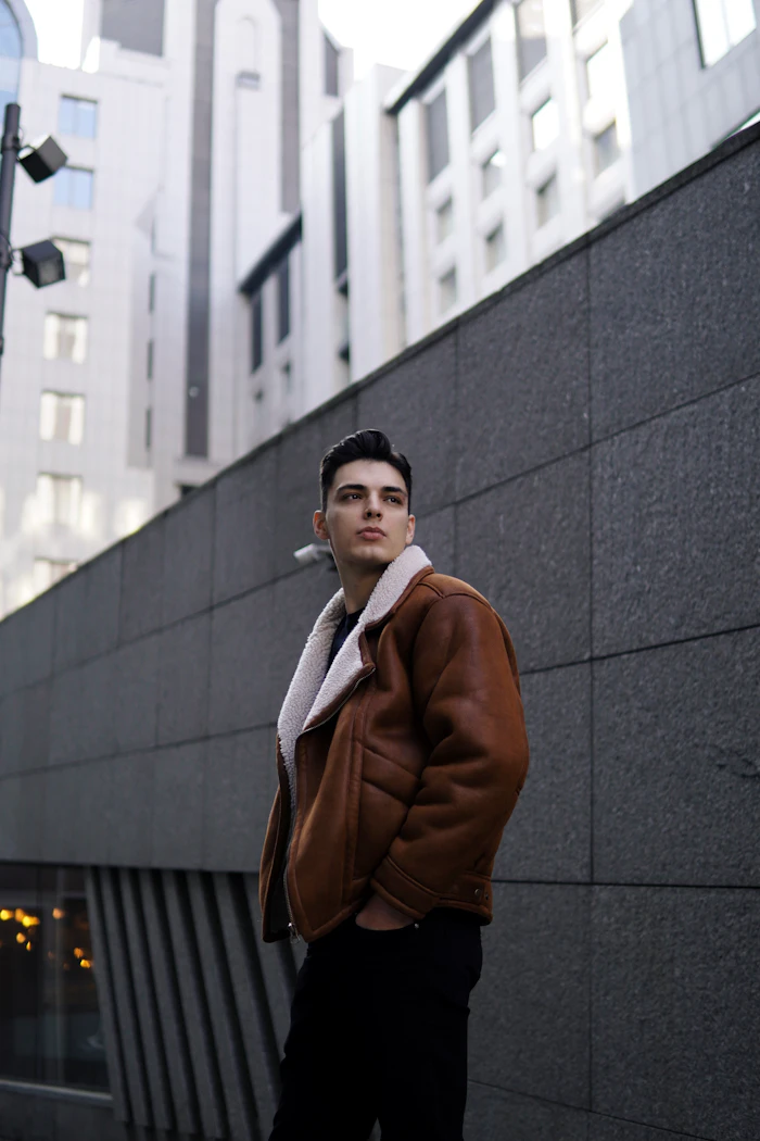 Man in a brown shearling flight jacket against a grey concrete wall