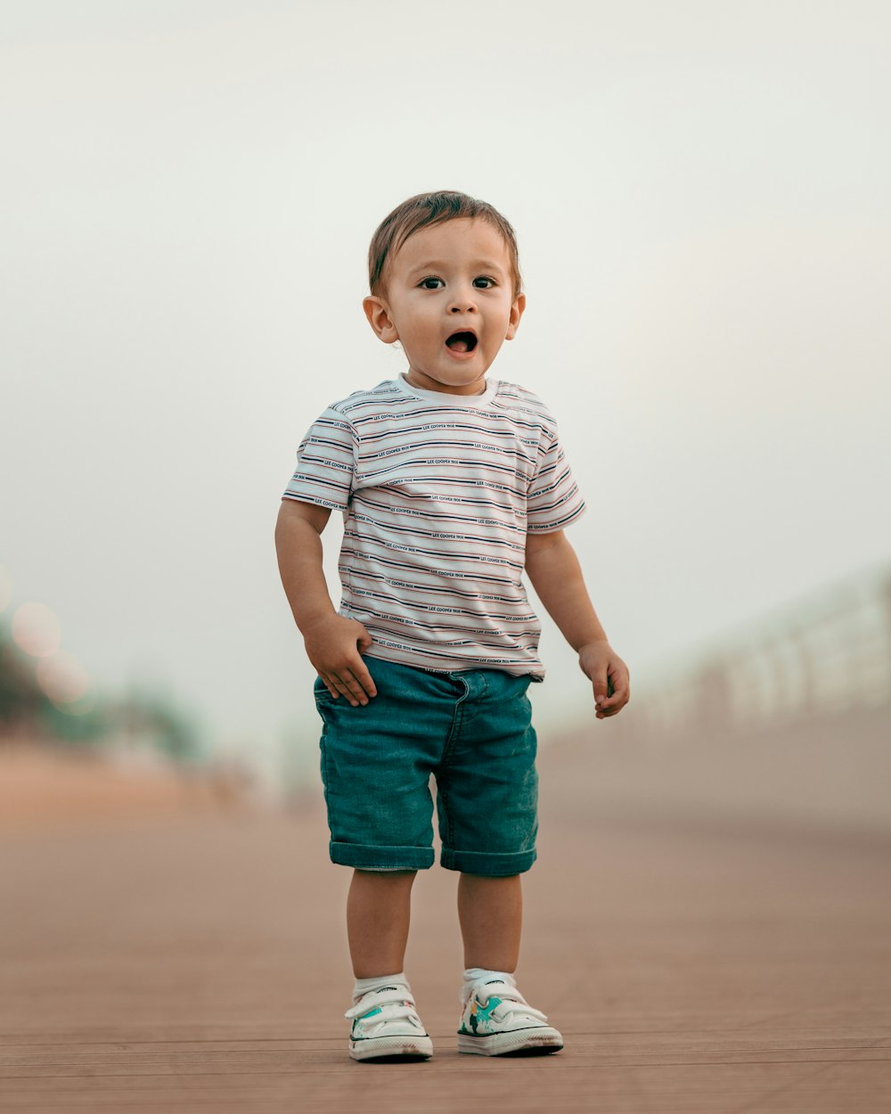 menino em branco e cinza listra t-shirt pescoço da tripulação e shorts jeans azuis em pé em cima sobre em sobre em