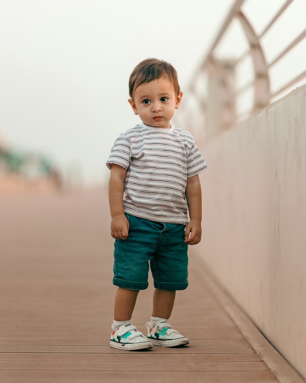 boy in white and gray striped t-shirt and blue denim shorts standing on brown wooden