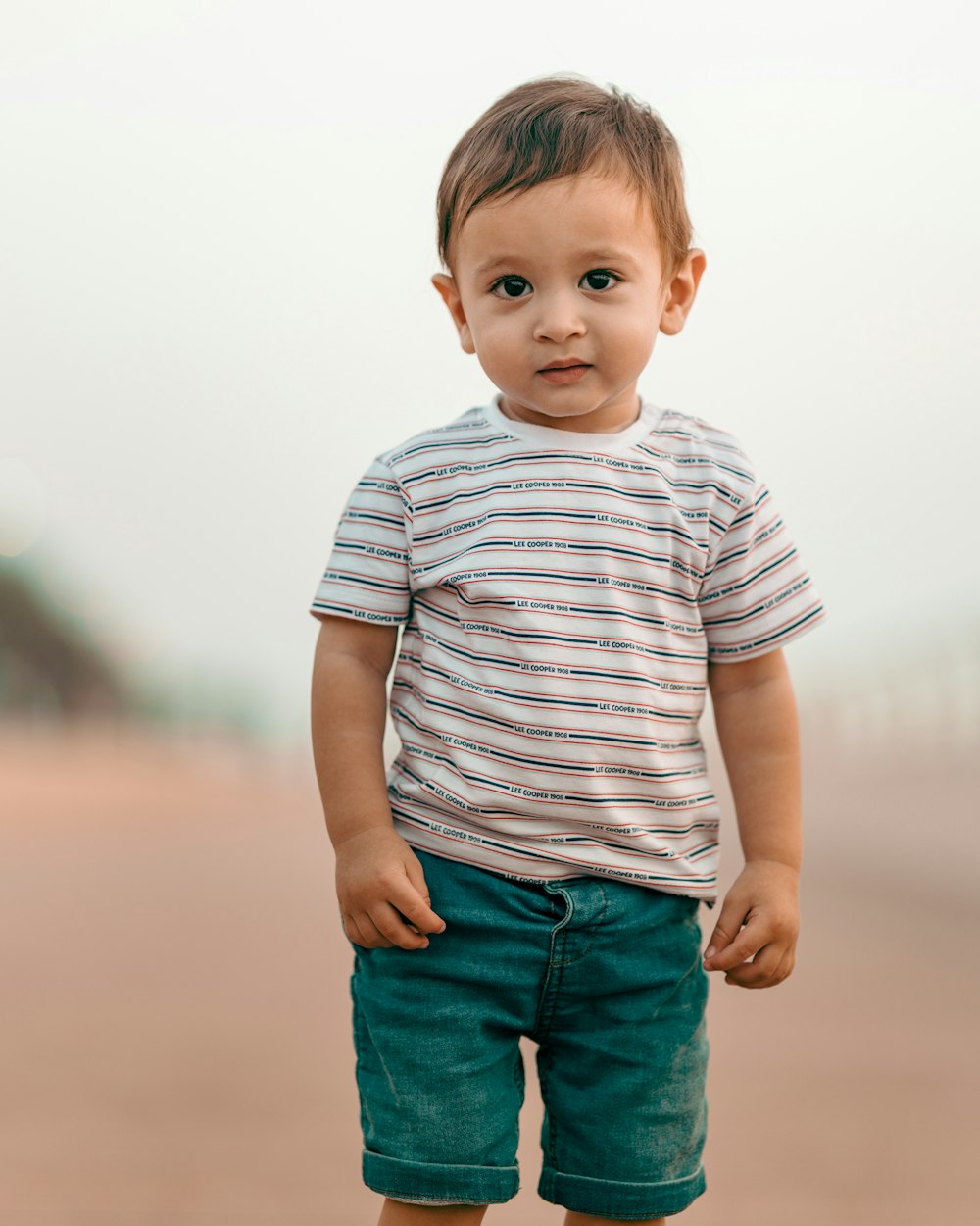 Niño con camiseta de cuello redondo a rayas blancas y grises y pantalones cortos de mezclilla azules