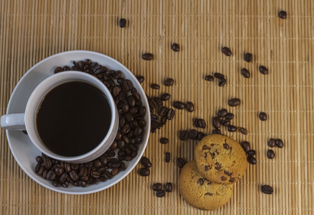 weißer Keramikbecher mit Kaffee neben braunen runden Früchten