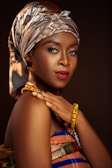 Portrait of a confident woman adorned in a red and green kente scarf against a black background.