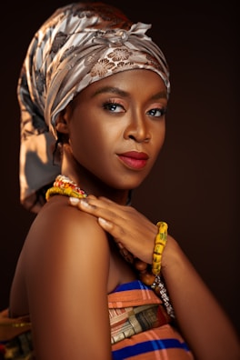 Portrait of a confident woman adorned in a red and green kente scarf against a black background.