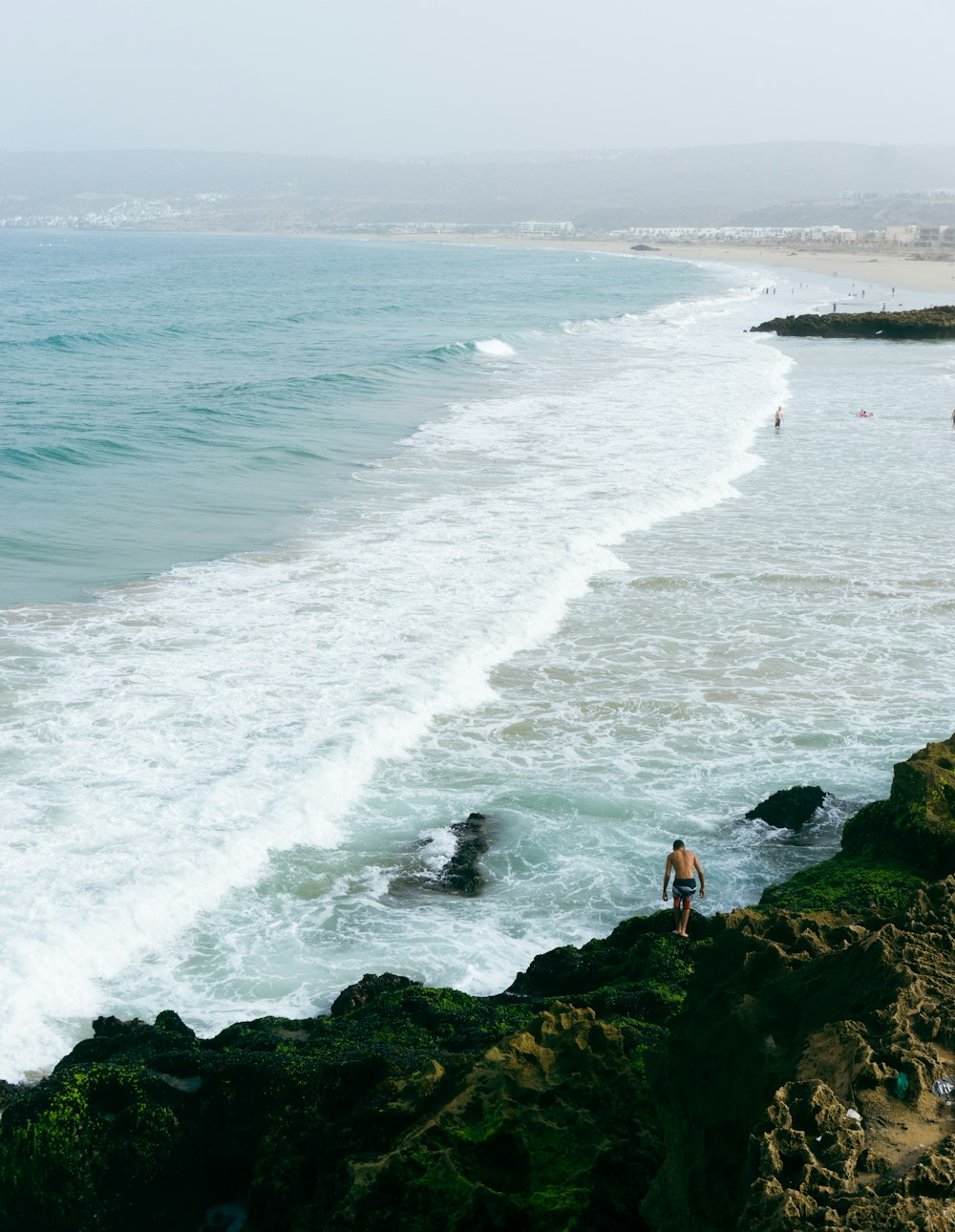 person standing on rock near sea waves crashing on shore during daytime