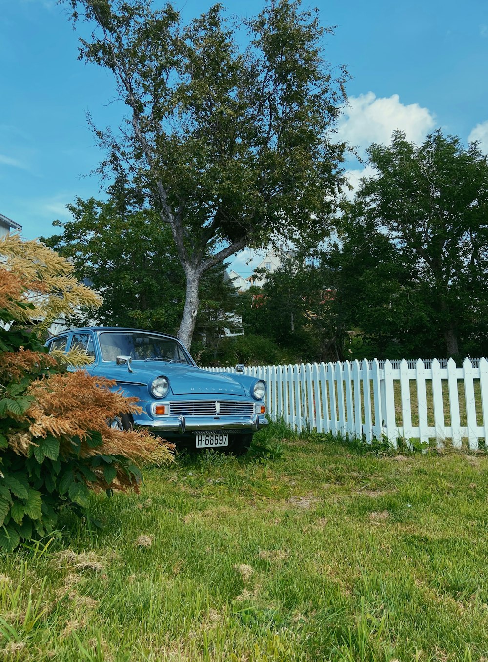 blue car parked beside white wooden fence during daytime