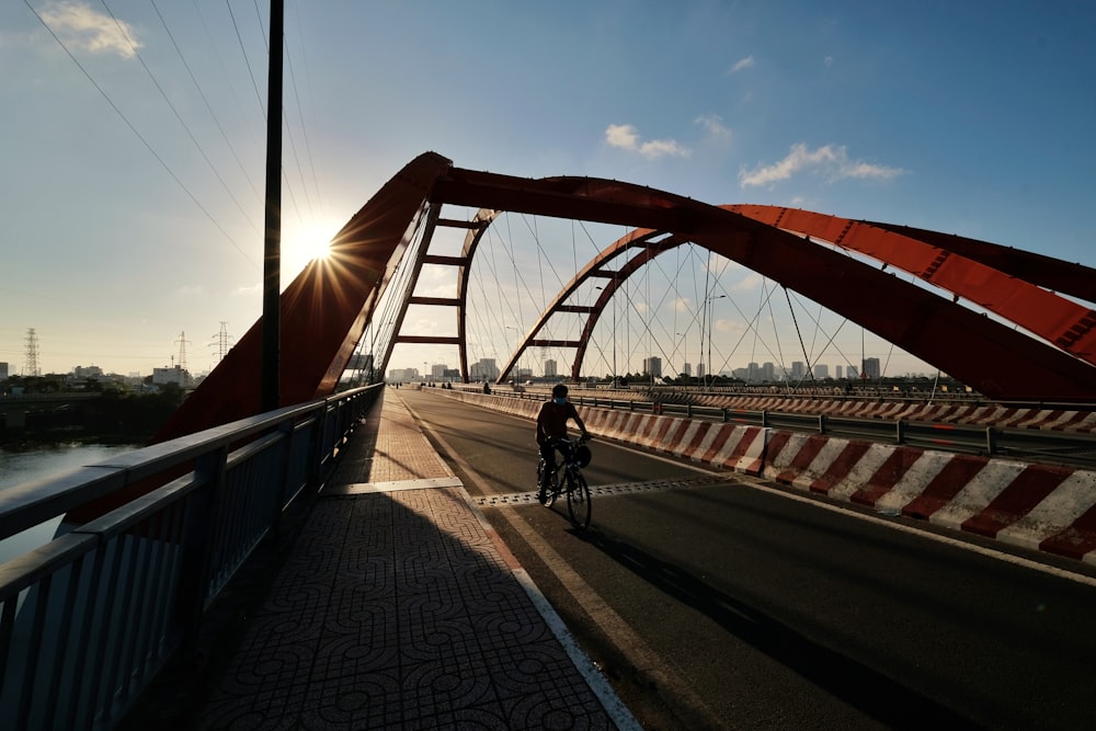 man in black jacket and black pants riding bicycle on bridge during daytime